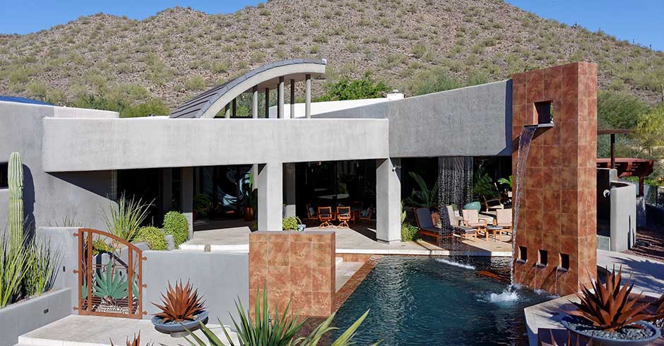 Modern Arizona home with infinity pool and waterfall, set against a barren mountain landscape with typical Arizona flora. An excellent example of a home that would benefit from a customized Arizona high value home insurance policy.