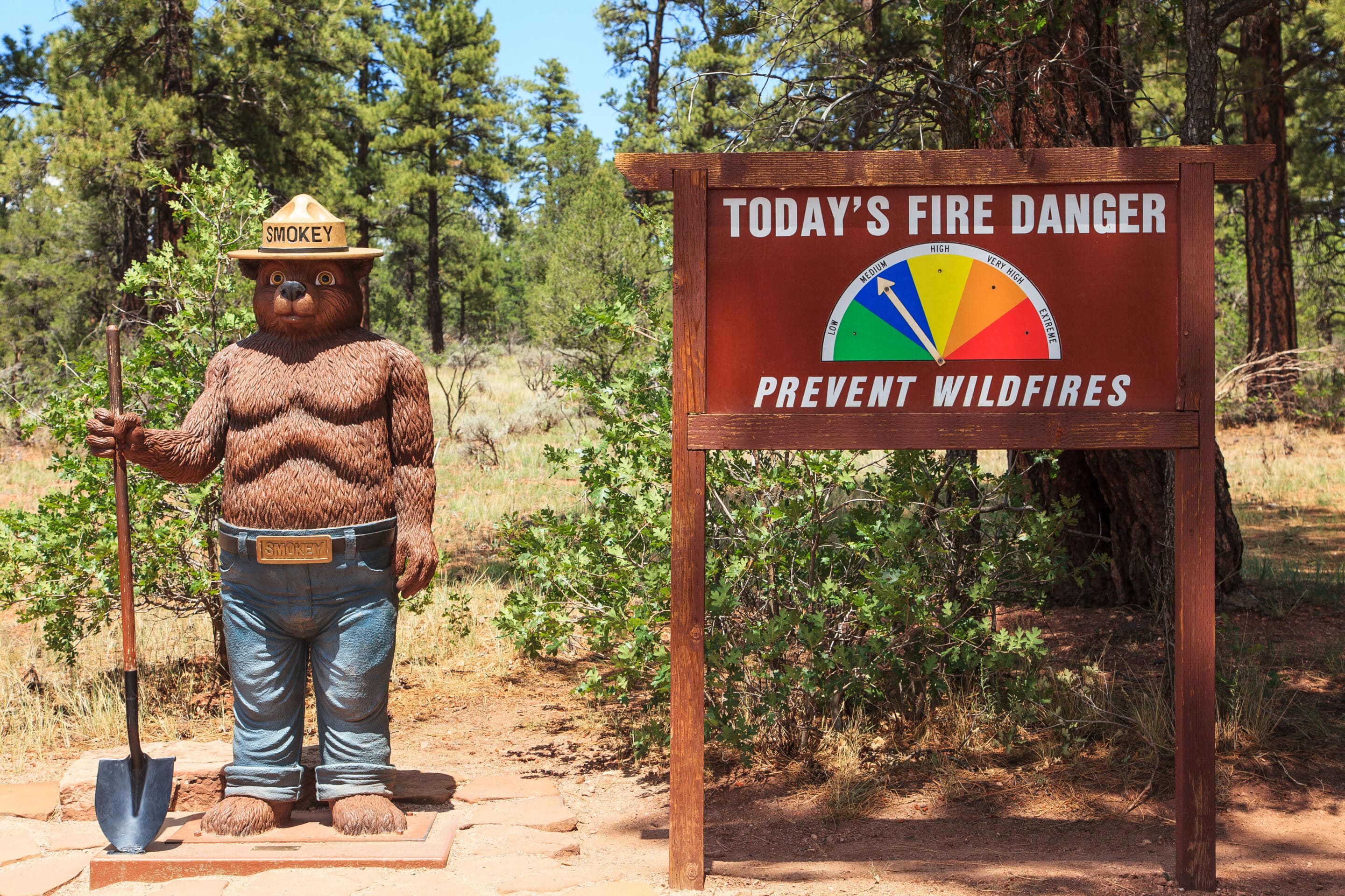 Statue of Smokey the Bear next to a 'Prevent Wildfire' sign and a fire danger scale at a trail entrance in Kaibab National Forest, Tusayan, Arizona. Wildfires are just one of many risks to take into account when building an Arizona high value insurance package.
