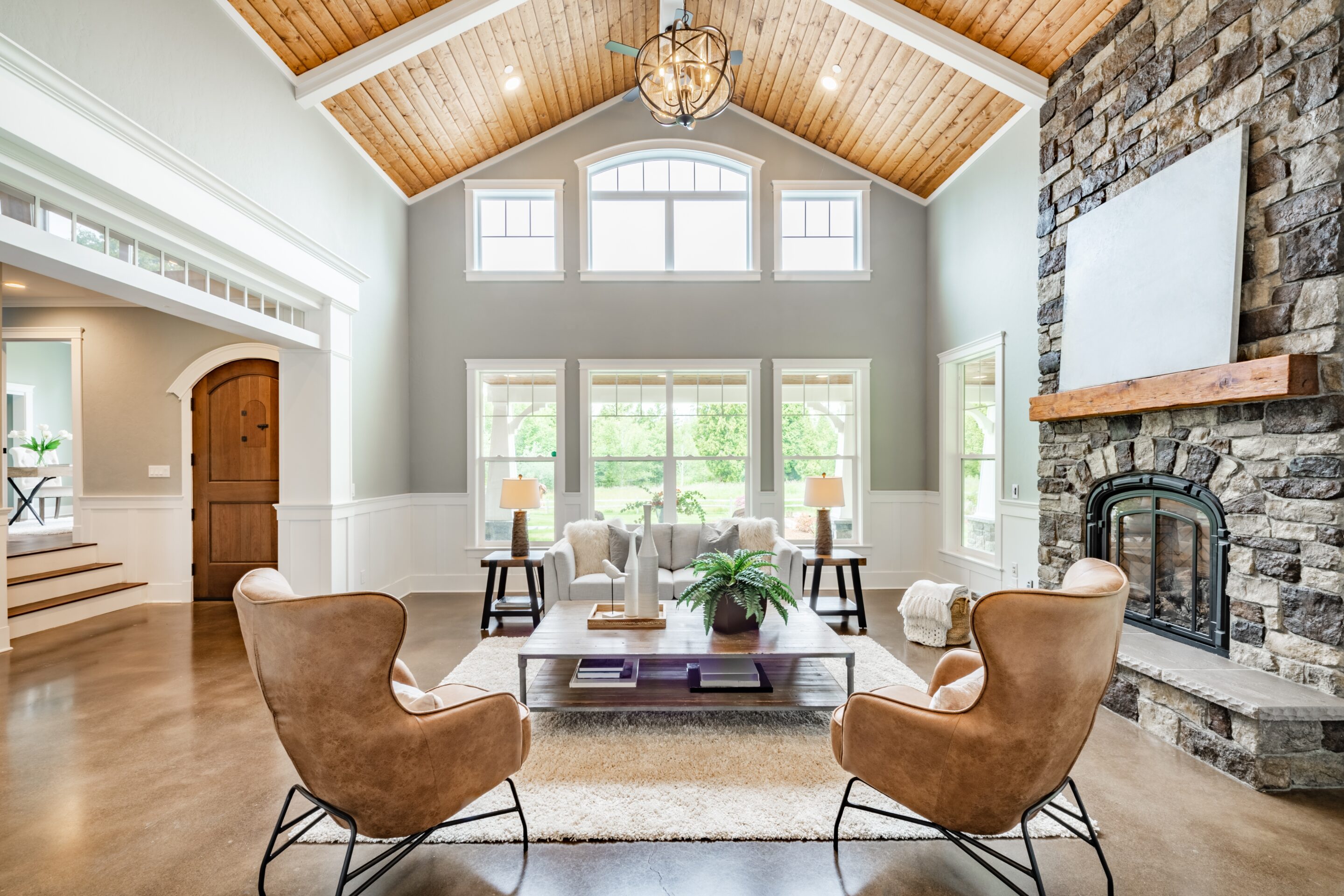 Luxurious living room in a high-end home, showcasing a modern design with a vaulted ceiling adorned with exposed wooden beams and a grand stone fireplace, embodying the sophistication and security covered by high end home insurance.