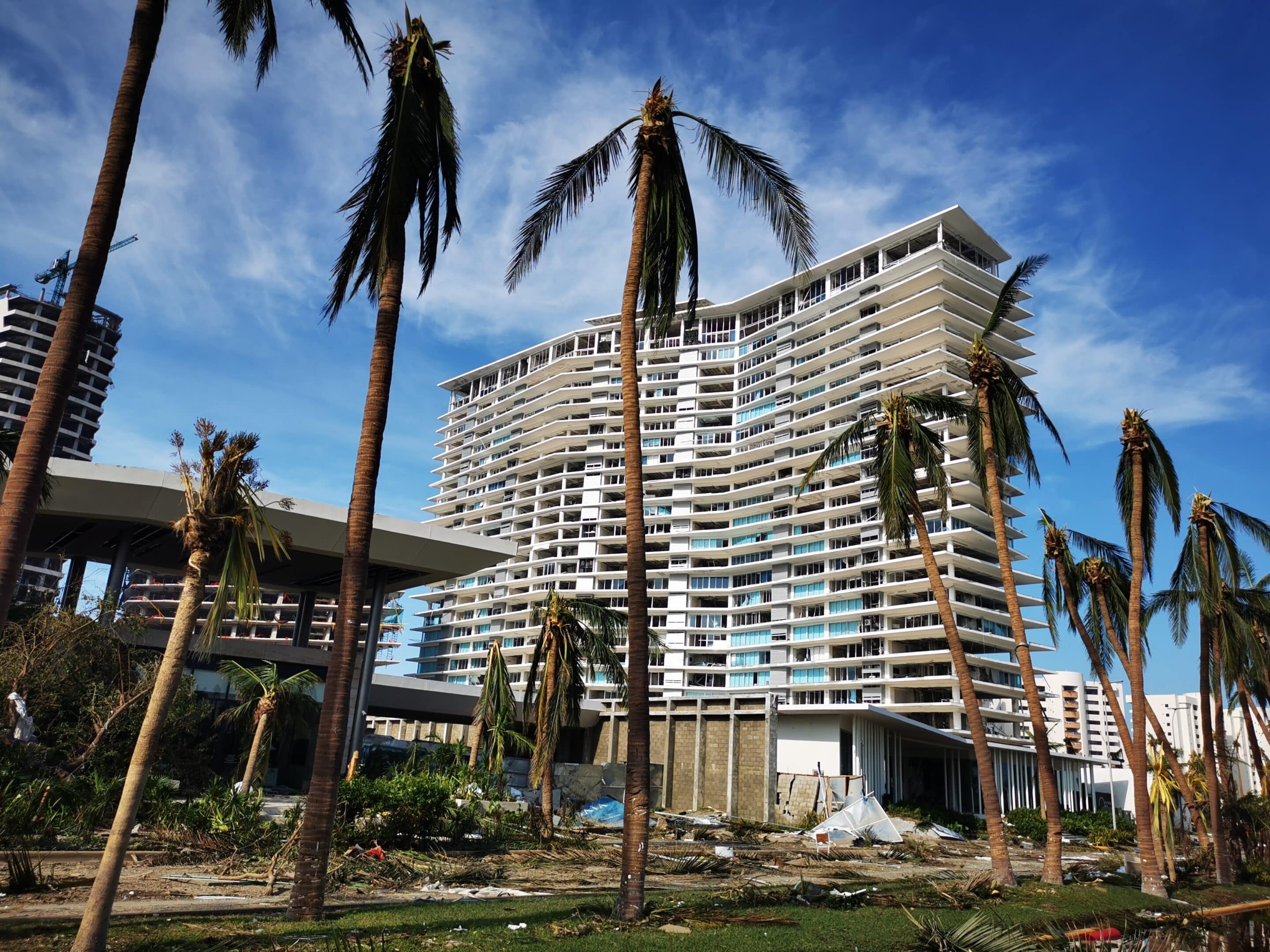 High-rise building with hurricane damage and bent palm trees, emphasizing the need for proper insurance preparation.