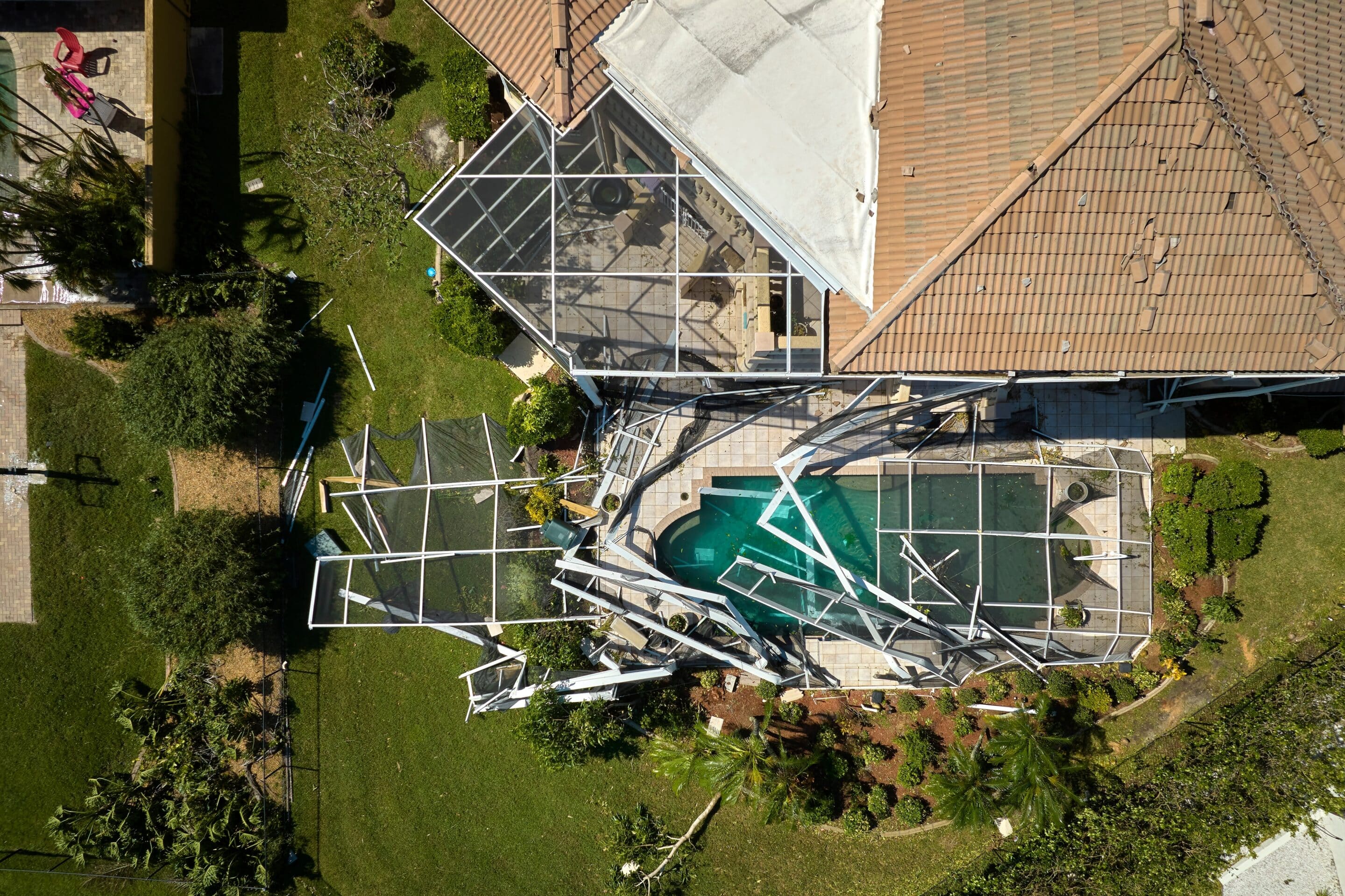 Aerial view of a home with hurricane damage to its screened enclosure, highlighting the importance of insurance preparation.