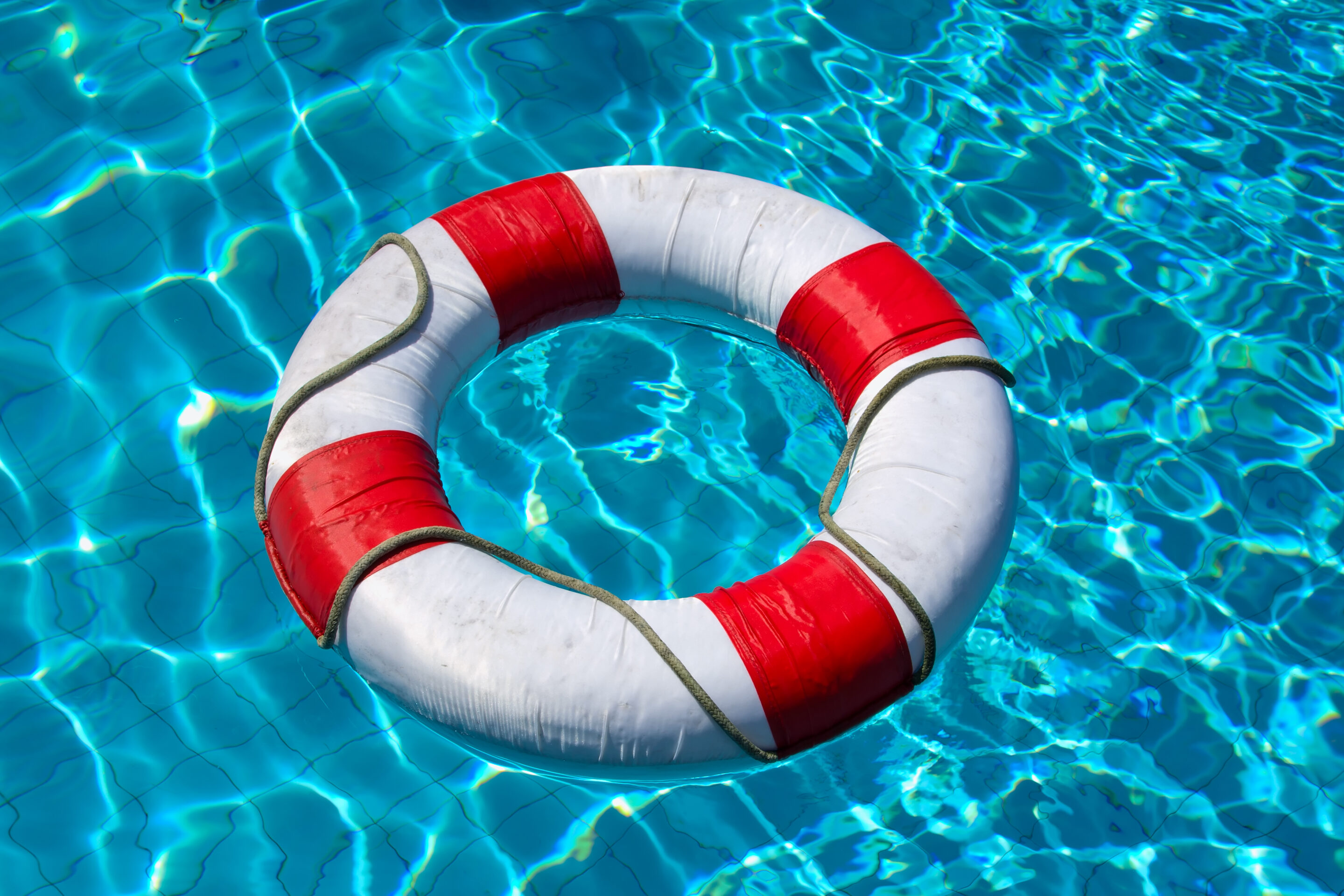 Red and white life buoy floating in a clear blue swimming pool, safety requirements are a large part of pool insurance.