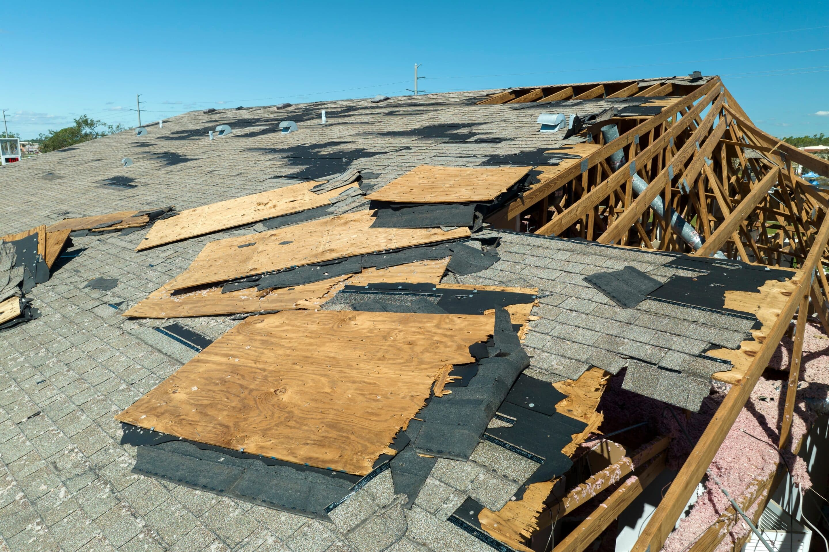 A damaged roof with exposed wooden trusses and torn shingles after a storm, underscoring the necessity of comprehensive home insurance in 2025.