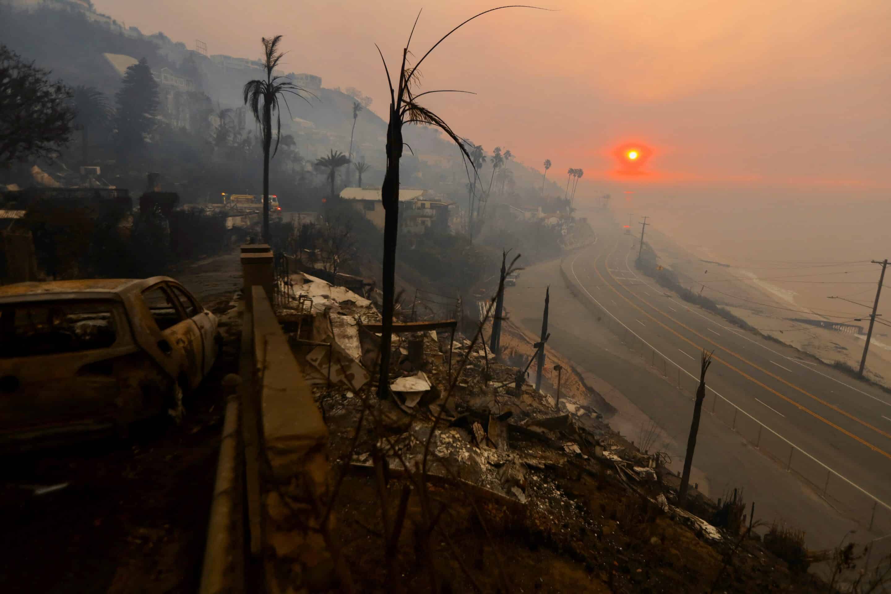 A wildfire-ravaged neighborhood with charred remains of homes, a burnt car, and a hazy orange sun in the background, emphasizing the importance of home insurance in 2025.