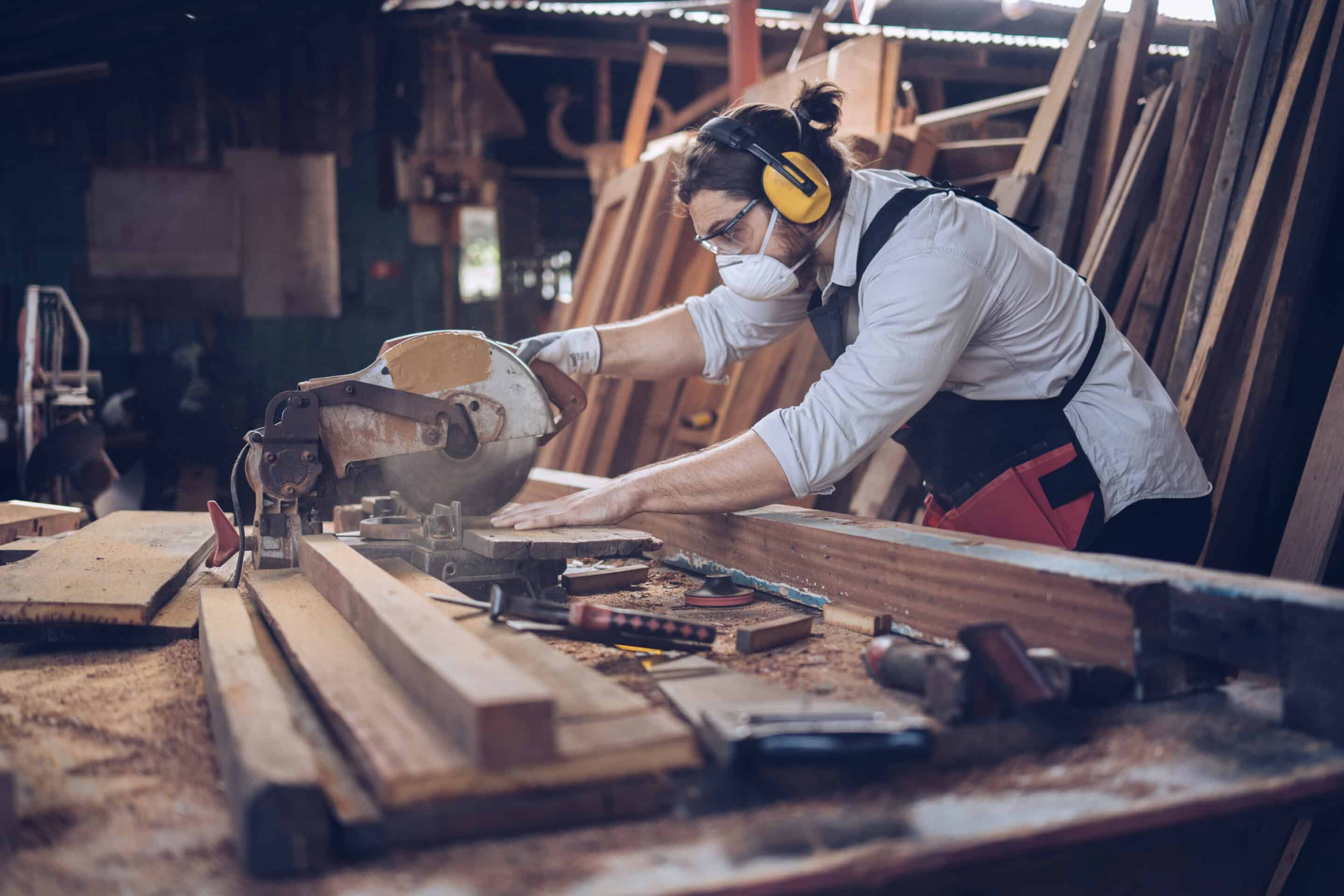 A woodworker wearing safety gear using a circular saw in a workshop, highlighting the need for business insurance in skilled trades.