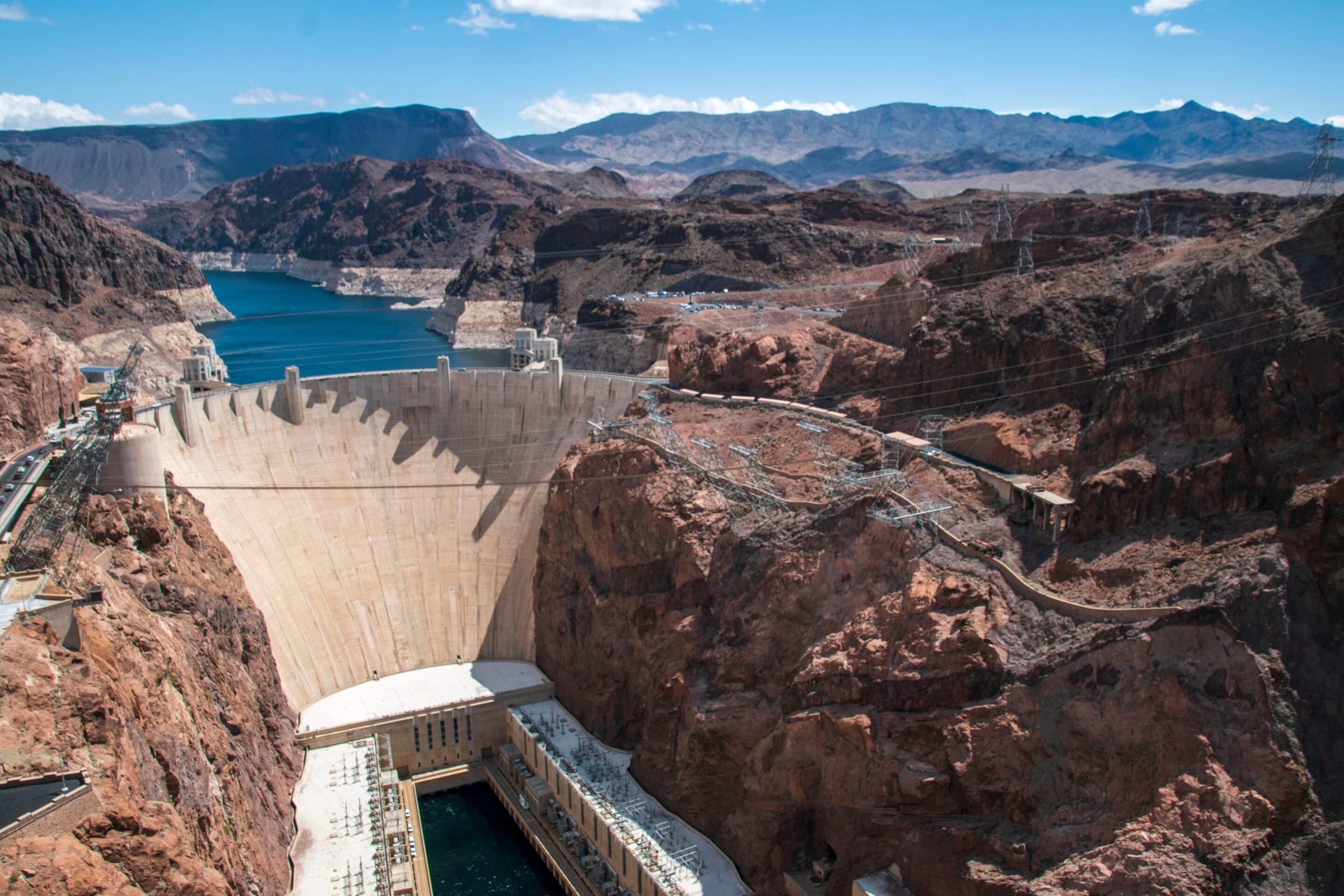 Hoover Dam holding back Lake Mead surrounded by desert mountains under blue sky.