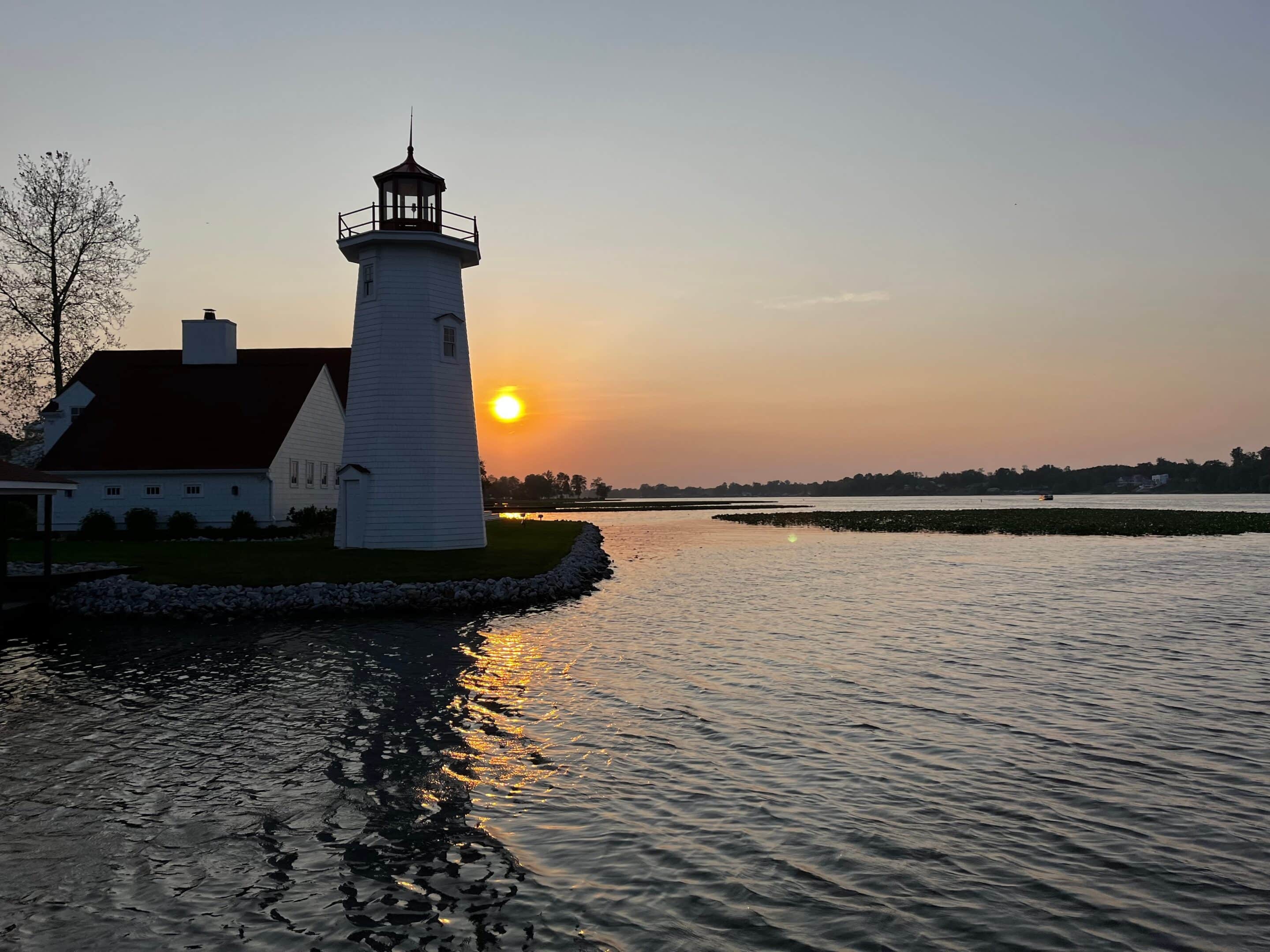 Silhouette of a lighthouse on the Lake Erie shore at sunset with calm waters and a glowing sky.