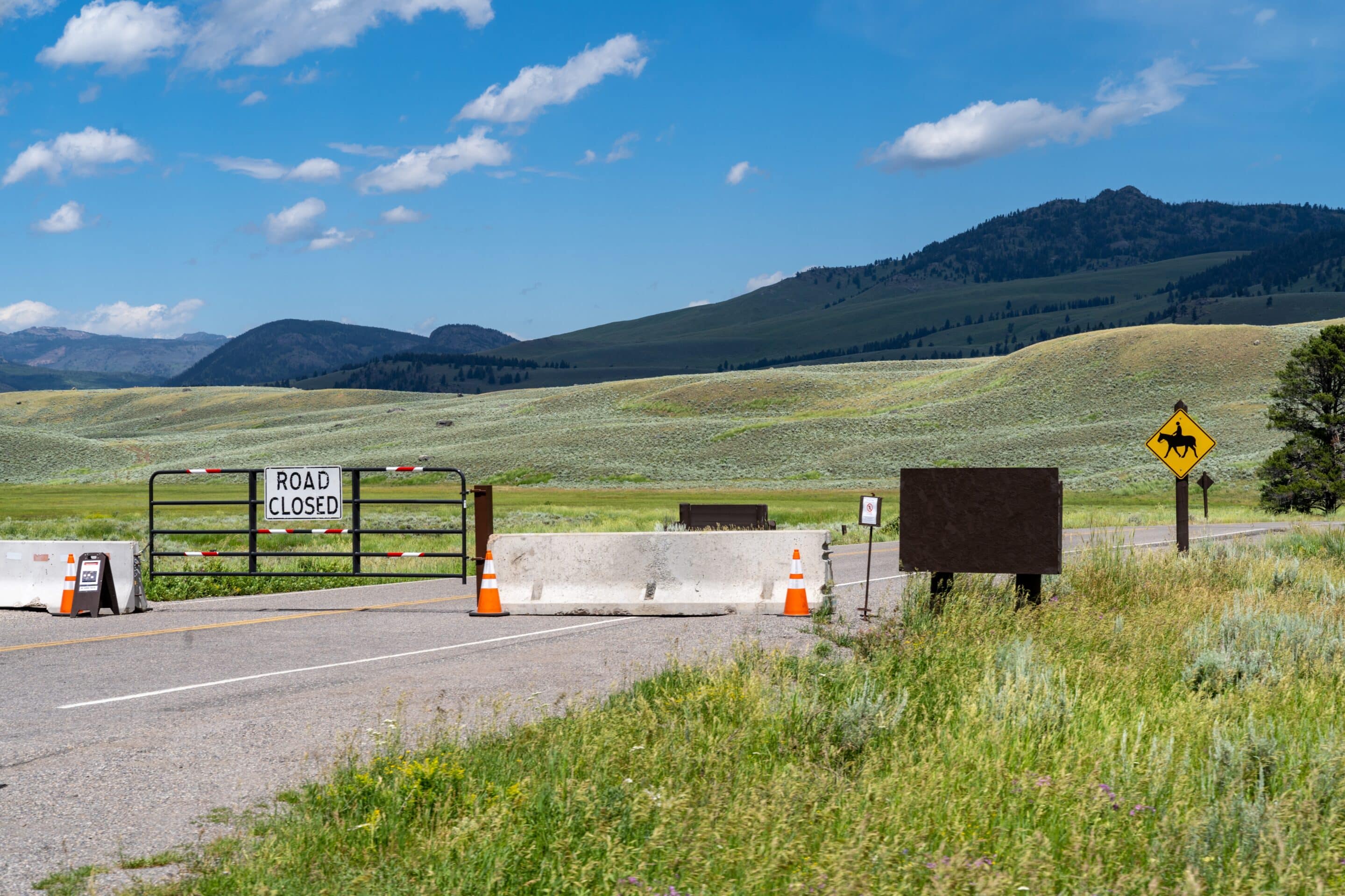 Road closed sign and barrier in an open Wyoming valley with distant hills and clear sky.