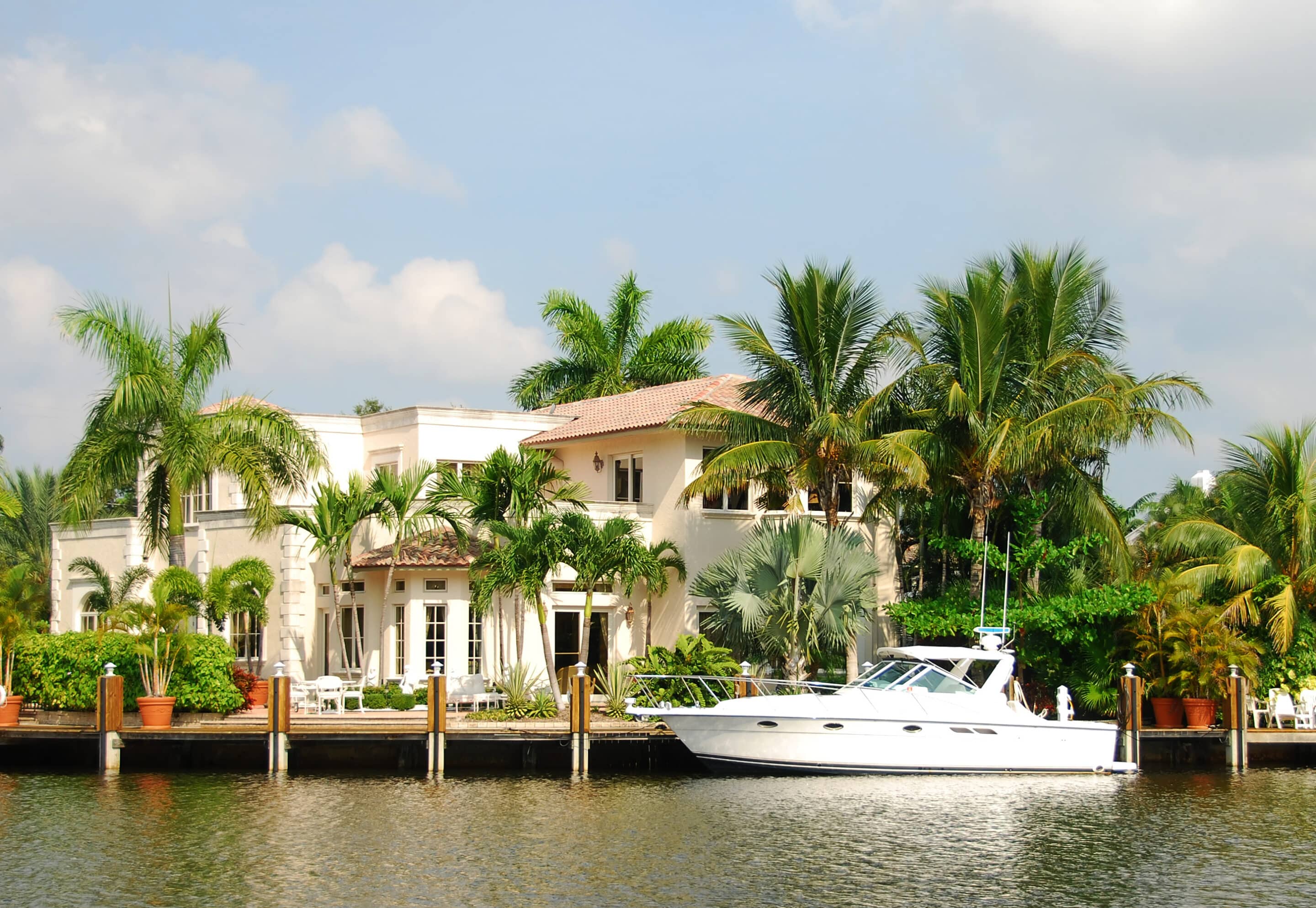 Waterfront mansion with docked yacht and palm trees — high value home insurance example.