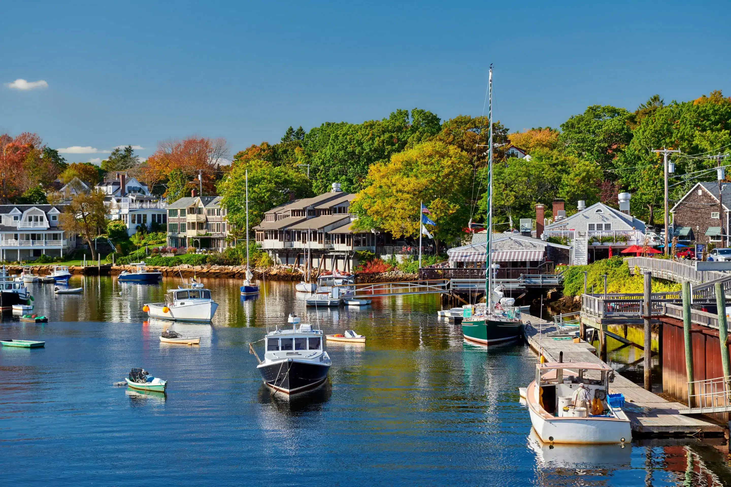 Picturesque harbor filled with boats, coastal homes, and colorful fall trees.