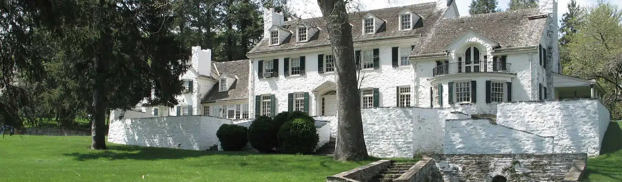 Elegant white mansion surrounded by lush green lawns and trees.